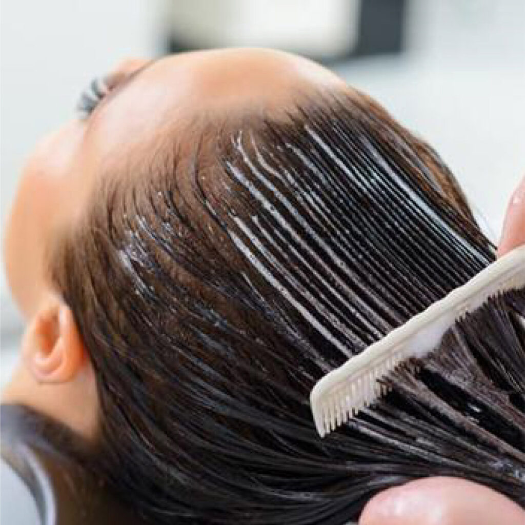 A woman getting conditioner combed through her hair