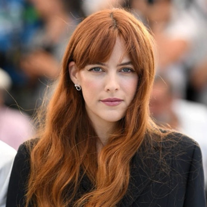 A woman with long wavy red hair and short bangs.