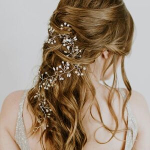 A half-up bridal hairstyle with a silver piece of jewelry intertwined in her hair.